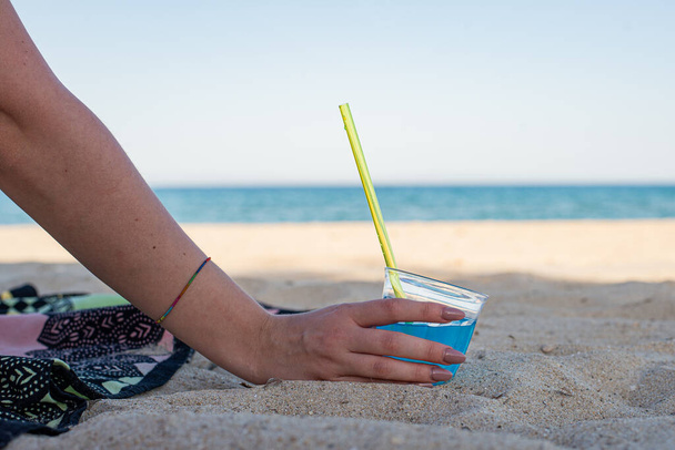Hand hält blaue Limonade auf Glas mit gelben Trinkhalmen am Ufer - Foto, Bild