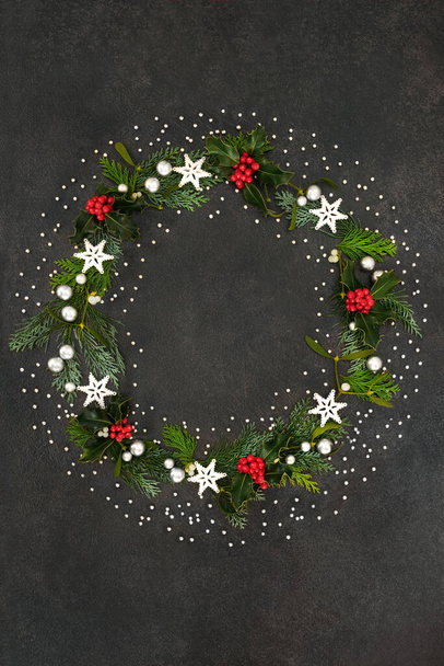 Karácsonyi koszorú csillag & ezüst labda dekoráció, magyal, fagyöngy & cédrus ciprusi fenyő grunge szürke háttér. Karácsonyi dekoráció az ünnepi szezonban. - Fotó, kép