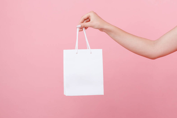 en la mano una bolsa blanca bajo el logotipo sobre un fondo rosa
 - Foto, Imagen