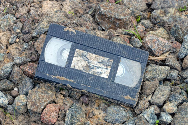 eine schwarze schmutzige alte Plastikvideokassette liegt auf grauen Steinen und Schutt auf der Straße - Foto, Bild