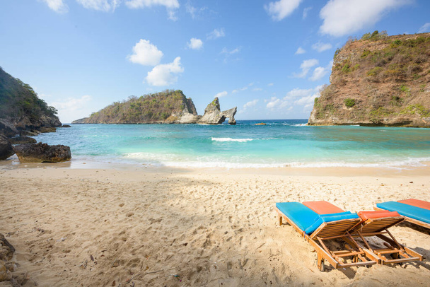 Популярна фотографія та туристичне місце Atuh Beach. Пустельний Лаунж крісла на тропічному піщаному пляжі, з морськими скелями і скелями на відстані, і бірюзовим морем в Нуса Пеніда, Балі, Індонезія. - Фото, зображення