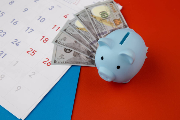 Czas zainwestować, koncepcja biznesowa. Niebieska świnka z banknotami, kalendarz na kolorowym tle - Zdjęcie, obraz
