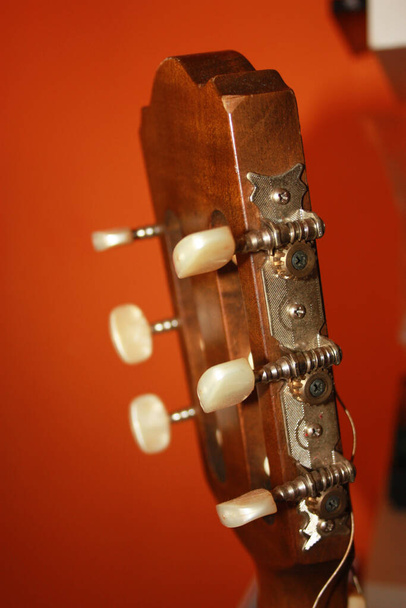 ヘッドストックにはオレンジを基調としたクラシックギターのメカニズムがあり - 写真・画像