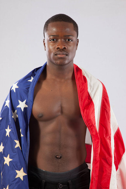 Красивый черный мужчина с обнаженной грудью и американским флагом, обернутым вокруг его плеч
. - Фото, изображение