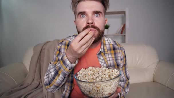 Home cinema concept. Shocked and scared man watching tv and eating popcorn - Metraje, vídeo