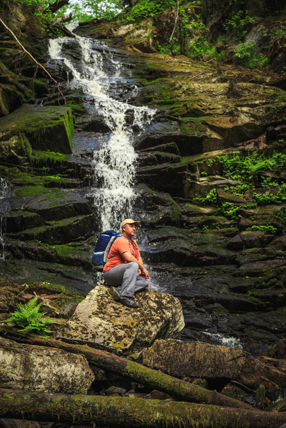 Tourist sits on a rock near a forest waterfall. Feeling of relaxation and freedom. - Foto, afbeelding