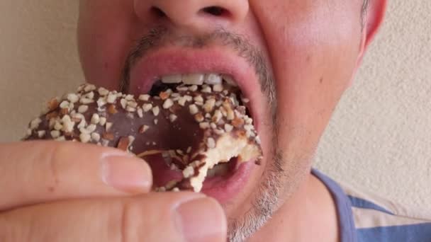középkorú, szakállas férfi fánkot eszik csoki cukormázzal. Portré. Közelkép. - Felvétel, videó