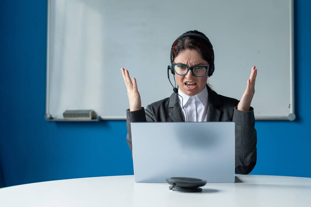 An angry woman in a headset is having an online conversation on a laptop in a conference room. Female boss scolding subordinates for a video call. Unsuccessful remote business negotiations. - Foto, immagini