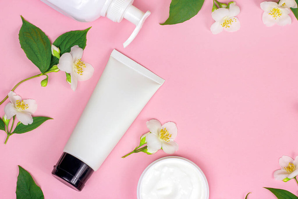 Top view of white plastic cosmetic container for moisturizing cream as a mock up with bright fresh jasmine flowers on light pink background with copy space. Body and skin care concept. - Photo, Image