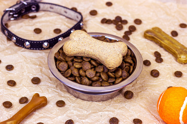 Brown biscuit bones and crunchy organic kibble pieces for dog feed with black collar on light background. Healthy dry pet food concept. - Photo, Image