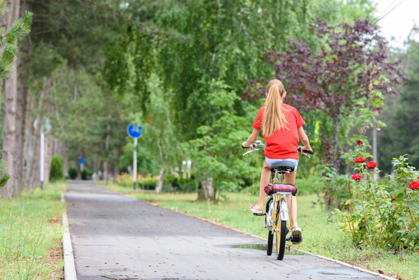 Dziewczyna w czerwonym T-shircie jeździ ścieżką rowerową w parku - Zdjęcie, obraz