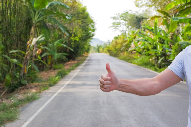 Travel, trip, vacation, wanderlust. Hitchhiker sign on road. Thumbs up male hand gesture outdoors. Hitchhiking, hitching, thumbing, auto stop concept. Happy vacation.Traveller on the way.Copy space - 写真・画像