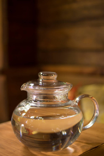 Egy átlátszó teáskanna vízzel áll egy fa tálcán. Jó éttermek, bannerek, plakátok, szórólapok. - Fotó, kép