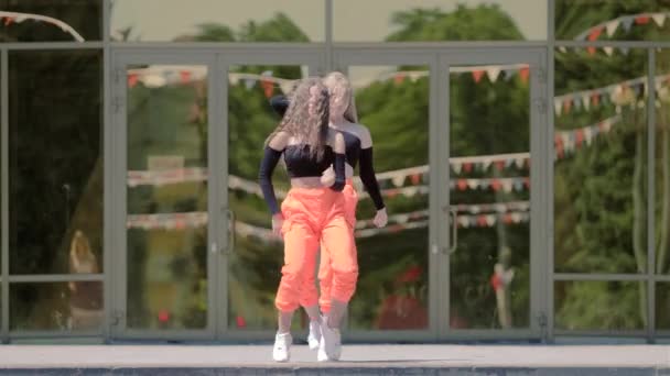 dwie młode kobiety z długimi włosami w dresie tanecznym twerk dancehall, uliczny taniec współczesny przed budynkiem. Taniec pupy - Materiał filmowy, wideo