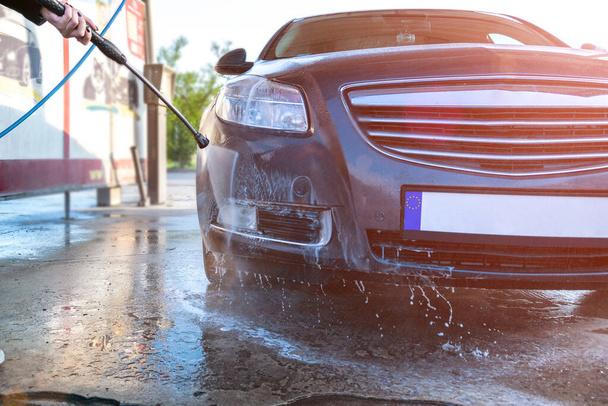 Woda czysty samochód na myjni ręcznej. Mycie pojazdów z mydła, piana na stacji czyszczącej. Ostrożnie z woskiem ciśnieniowym. - Zdjęcie, obraz