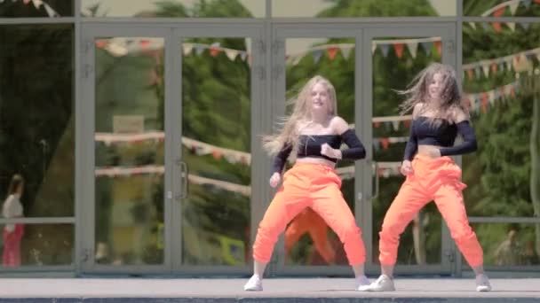 twee jonge vrouwen met lang haar in trainingspak dansen danszaal twerk, straat moderne dans voor het gebouw. Booty Dance. Langzame beweging - Video