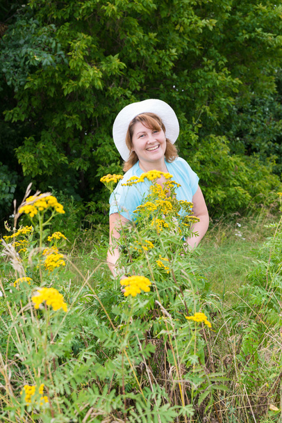Middle-aged woman on a meadow with tansy - Foto, afbeelding