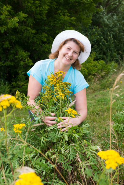 Middle-aged woman on a meadow with tansy - Foto, afbeelding