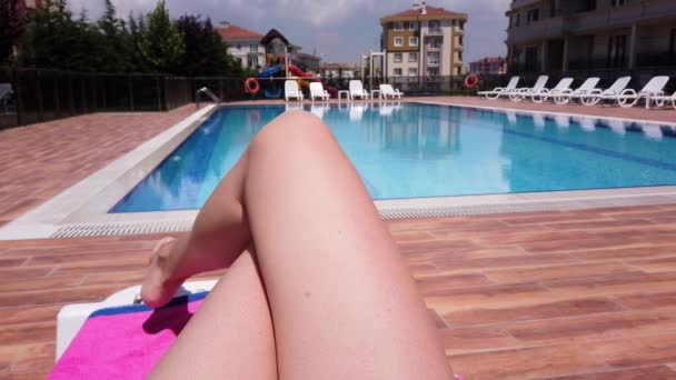 Benen van een blanke jonge vrouw. Een close-up. vrouw ligt zonnebaden tegenover zwembad. - Video