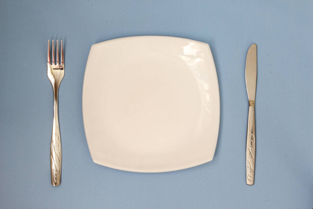 Empty plate, fork and knife over blue background. Clean plate and cutlery on light background. Top view. - Valokuva, kuva