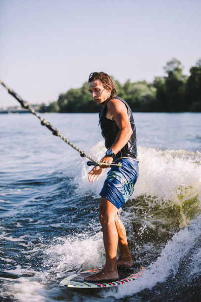 Aktív ébrenlét ugrás a ébrenléti fedélzeten lefelé a folyó hullámain. Hullámos szörfözés. Férfi atléta edzés a Wakesurf edzésen. Aktív vízi sportok a fedélzeten. Egy férfi hullámot fog szörfözés közben.. - Fotó, kép