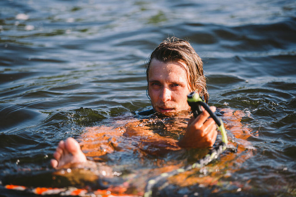 Gyönyörű hosszú hajú szőke mellényben ébred a tó hullámai mentén. A sportoló férfi sportoló nyáron szörfözik a folyón. Wakesurf vízi sport. Hullámos szörfözés. Ember szörfözik a szörfdeszkán. - Fotó, kép