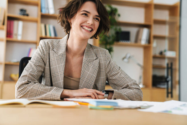 Beautiful smiling young businesswoman sitting at the office desk - Foto, Imagem