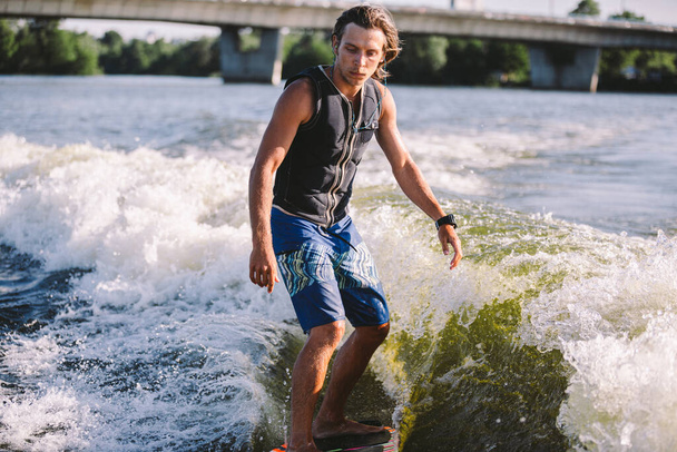 Actieve wakesurfer springt op wakeboard langs de riviergolven. Surfer op golf. Mannelijke atleet training op wakesurf training. Actieve watersporten in de open lucht aan boord. Een man vangt een golf op de branding. - Foto, afbeelding