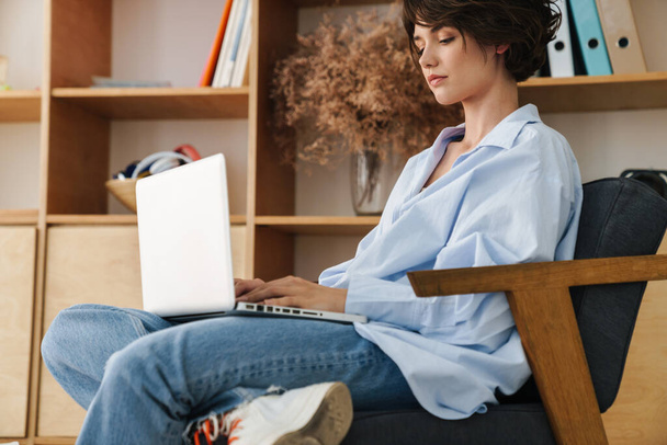 Magabiztos fiatal vonzó nő vállalkozó ül a széken az irodában, dolgozik laptop számítógép - Fotó, kép