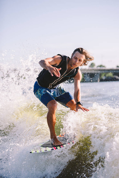 Ein Mann surft auf einem Surfbrett, das von einem Motorboot über der Welle des Bootes gezogen wird. Weixerfer beschäftigt sich mit Surfen, Unterhaltung, Freizeit, Wassersport. Athlet gleitet auf den Wellen auf dem Brett. - Foto, Bild