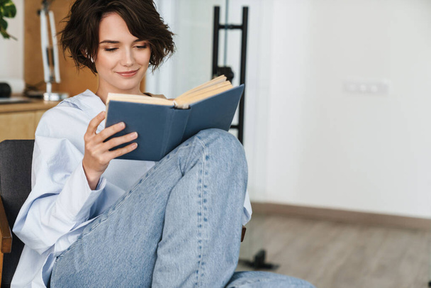 Sorridente giovane donna imprenditore lettura libro mentre seduto in ufficio - Foto, immagini