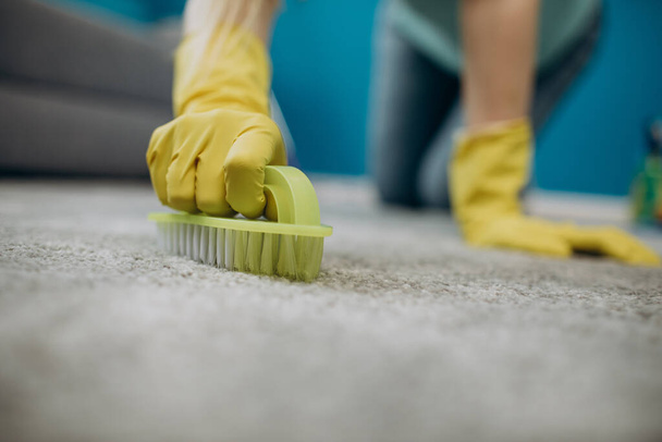 Primer plano de ama de casa en guantes limpieza alfombra con cepillo
 - Foto, imagen