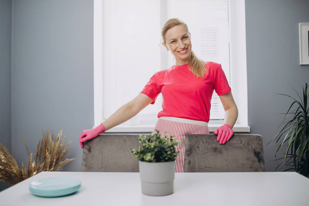 Beautiful woman in apron and gloves standing on cozy kitchen - Foto, imagen