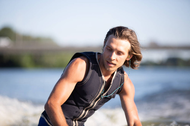 Uzun saçlı genç atletik adam güneşli yaz havasında nehir dalgalarında uyanıyordu. Yazın açık hava aktiviteleri. Su sporları kurulda uyanış yapıyor. Su sıçramasında kayan wakeboardçu. - Fotoğraf, Görsel