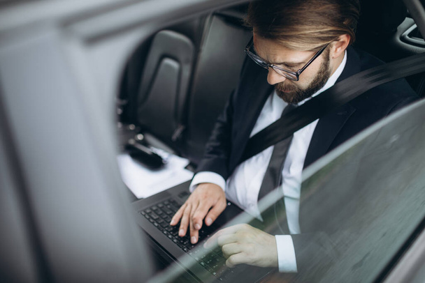 Liikemies työskentelee kannettavan tietokoneen kanssa ajaessaan autossa - Valokuva, kuva