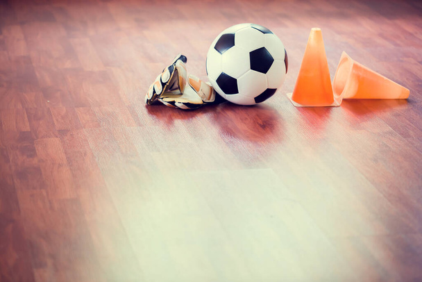 Soccer ball , gloves and marker cones are on wooden futsal floor. Equipment for training of Indoor soccer sports. Futsal training equipment on the wooden floor. - Photo, Image