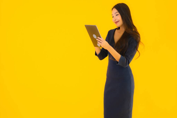Portret mooie jonge aziatische vrouw met slimme tablet elektronisch op geel geïsoleerde achtergrond - Foto, afbeelding