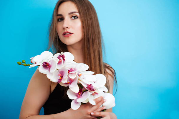 Young woman holding orchid flower on white background in studio. The girl looks at the camera. Close up - Zdjęcie, obraz