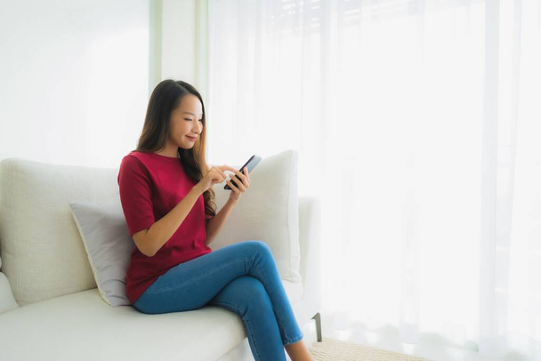 Ritratto belle giovani donne asiatiche utilizzando cellulare o smart phone sul divano in salotto interno
 - Foto, immagini