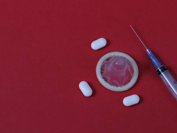kondomi, ruisku ja kolme pilleriä oikealla punaisella paperilla taustalla ja tekstipaikka oikealla, lähikuva virheestä. - Valokuva, kuva