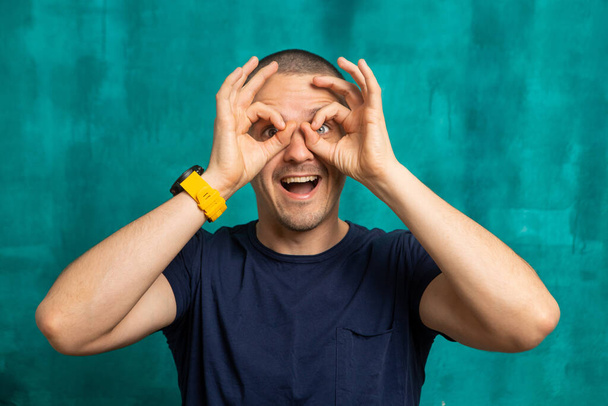 Divertido hombre riendo mirando en la cámara y haciendo gafas por las manos
. - Foto, Imagen