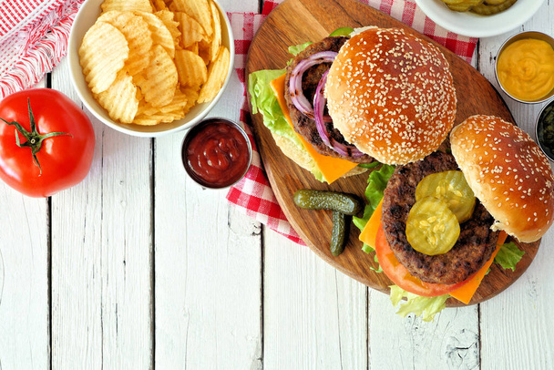 BBQ hamburgers met chips. Overhead view tafel scene op een witte houten achtergrond. - Foto, afbeelding