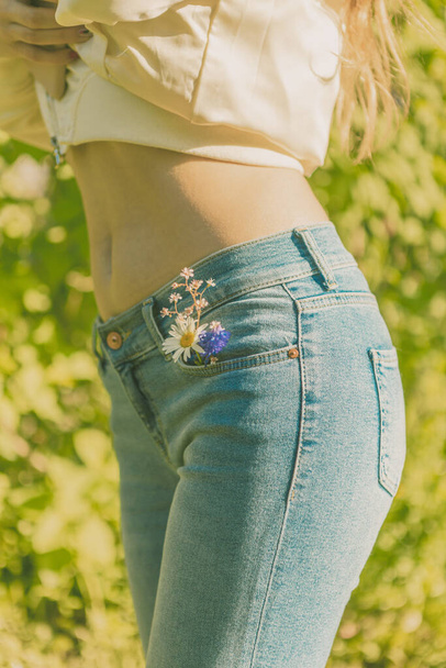 Beautiful girl in blue jeans with a camomile in her pocket. Walk in the green park. - Φωτογραφία, εικόνα