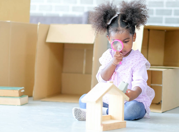 Афроамериканська маленька дівчинка грає зі збільшувальним склом і домашньою моделлю з картонним фоном. Концепція щастя і веселощів з іграшками для навчання нових знань.. - Фото, зображення