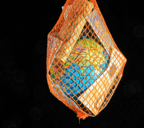 Globe trapped in a green net with euro currency on a dark black bacground - Photo, Image