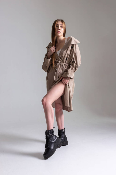 attractive caucasian skinny girl in raincoat posing on white studio cyclorama - 写真・画像