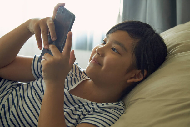Little girl enjoys using mobile phones on the sofa at home. - Photo, image