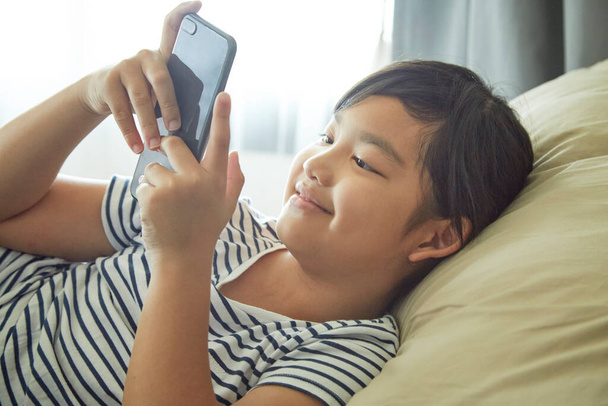 Little girl enjoys using mobile phones on the sofa at home. - Foto, afbeelding