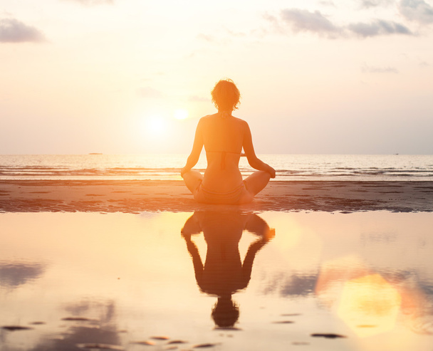 Femme de yoga assis dans la pose de lotus sur la plage pendant le coucher du soleil
 - Photo, image