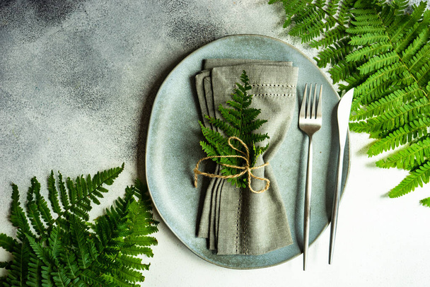 Καλοκαιρινό αγροτικό τραπέζι με πιάτο και μαχαιροπήρουνα διακοσμημένα με φρέσκα φύλλα φτέρης σε πέτρινο φόντο με χώρο αντιγραφής - Φωτογραφία, εικόνα